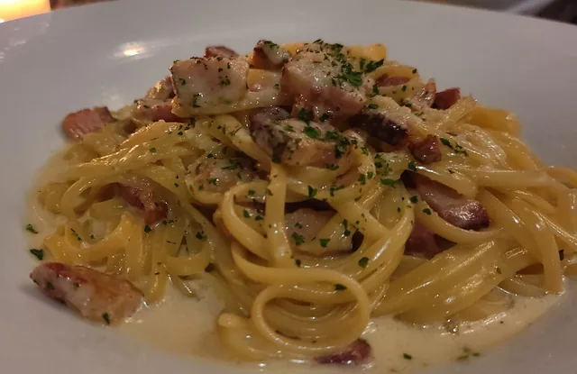 Creamy long pasta with herbs and diced meat on a white plate