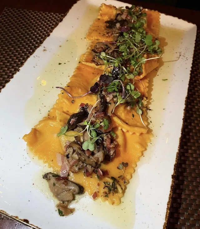 Filled pasta topped with mushrooms and greens on a rectangular plate