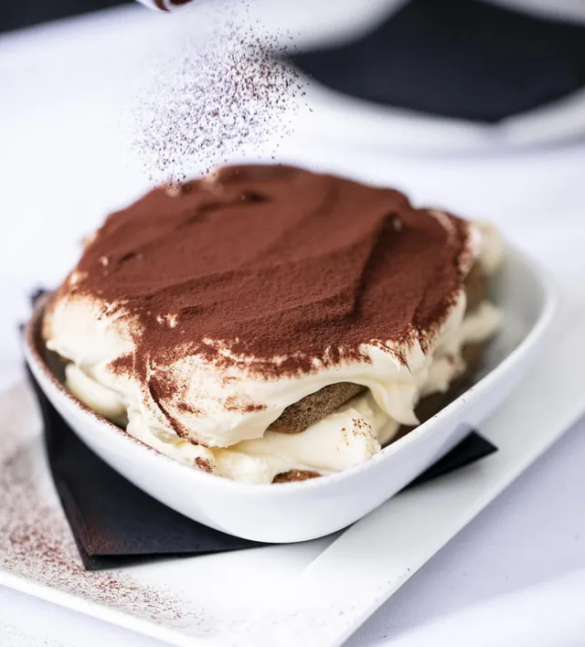 Tiramisu topped with cocoa in a white bowl
